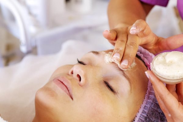 Cosmetologist applies  a moisturizing mask on female face. Woman in a spa salon on cosmetic procedures for facial care.  White woman getting beauty treatment therapy.