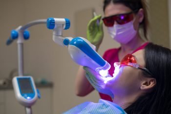 Close-up portrait of a female patient at dentist in the clinic. Teeth whitening procedure with ultraviolet light UV lamp.