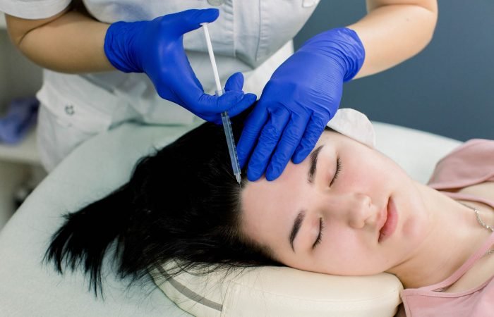 Hair mesotherapy or hair transplant: a beautician doctor makes injections in the head of a woman for hair growth or to prevent baldness.