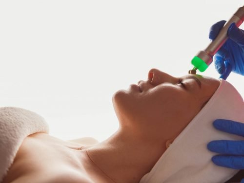 Young woman getting ultrasound skin cleansing and face treatment at beauty salon. Beautician takes care of her face